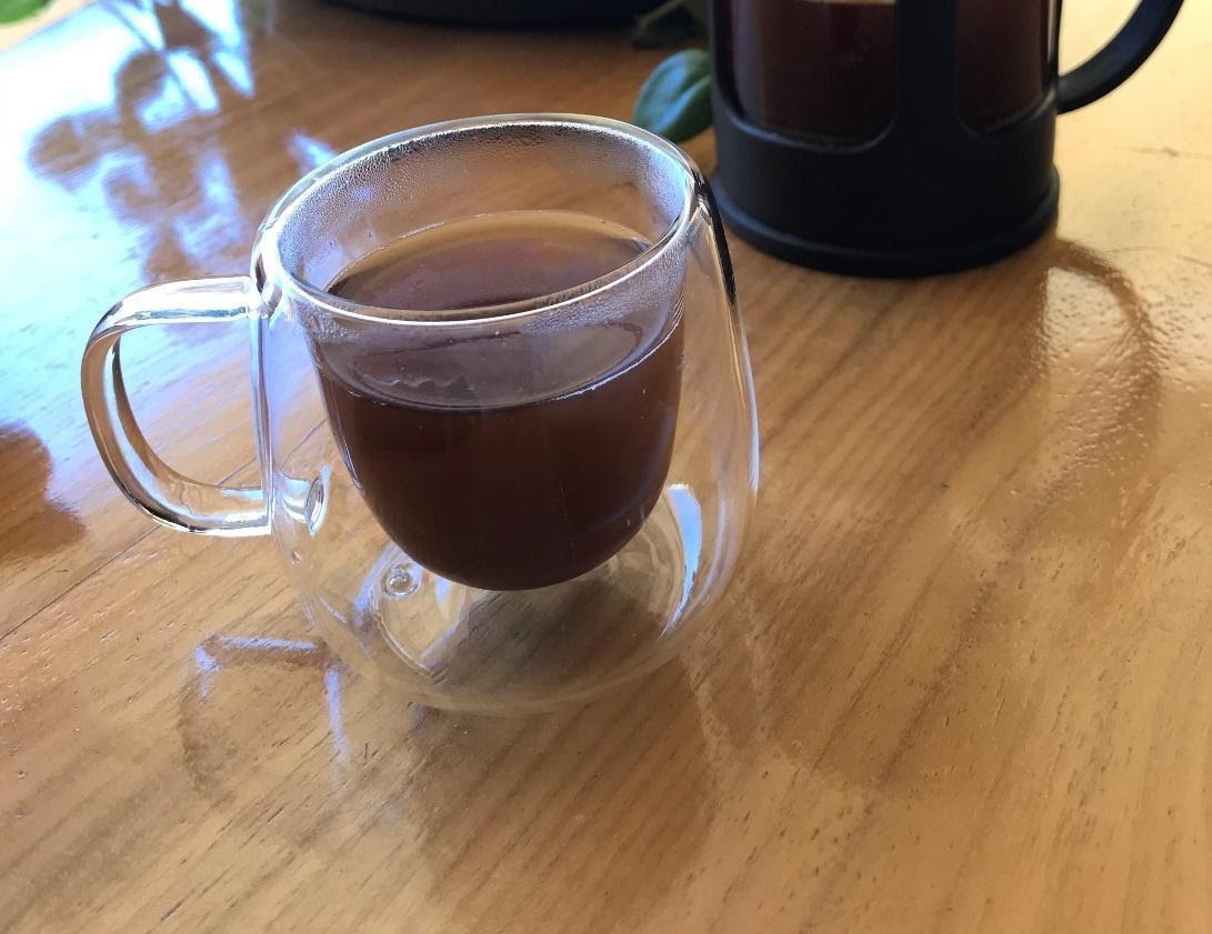 Xícara transparente com café em cima de uma mesa.